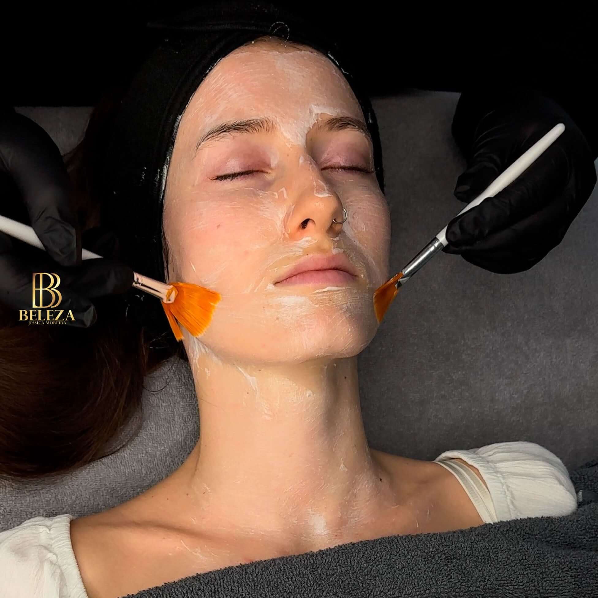 Woman receiving a facial treatment with brushes and cream at a beauty salon, showcasing skincare routine.