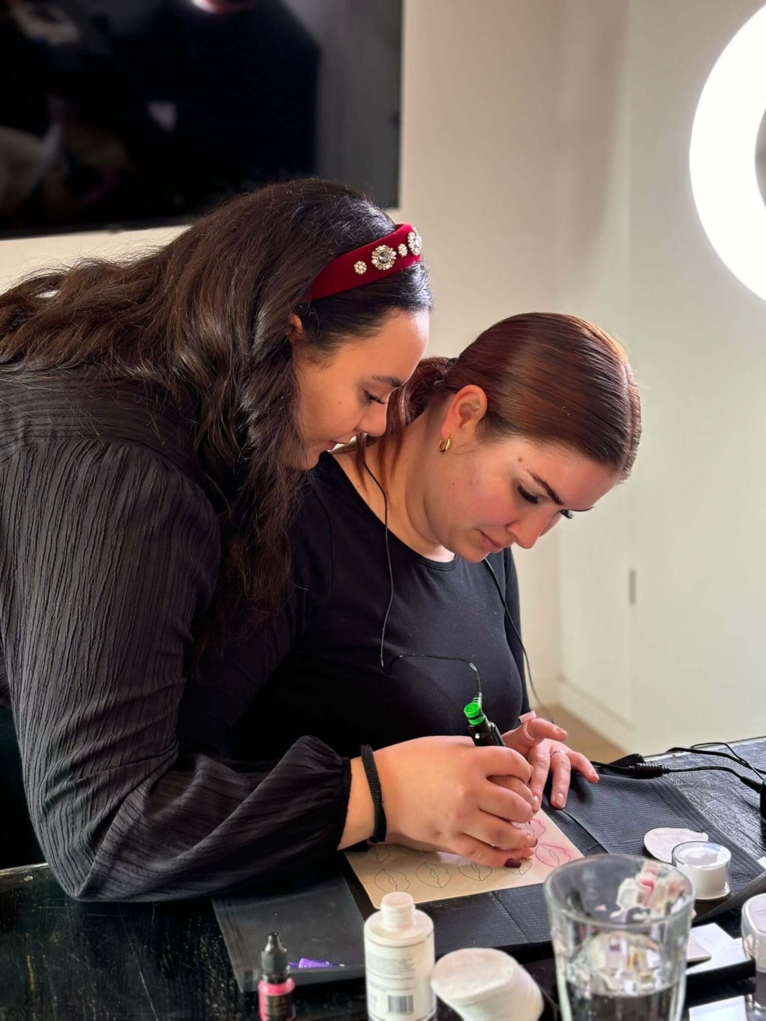 Two women engaged in a creative session, one teaching the other nail art techniques at a stylish workspace.