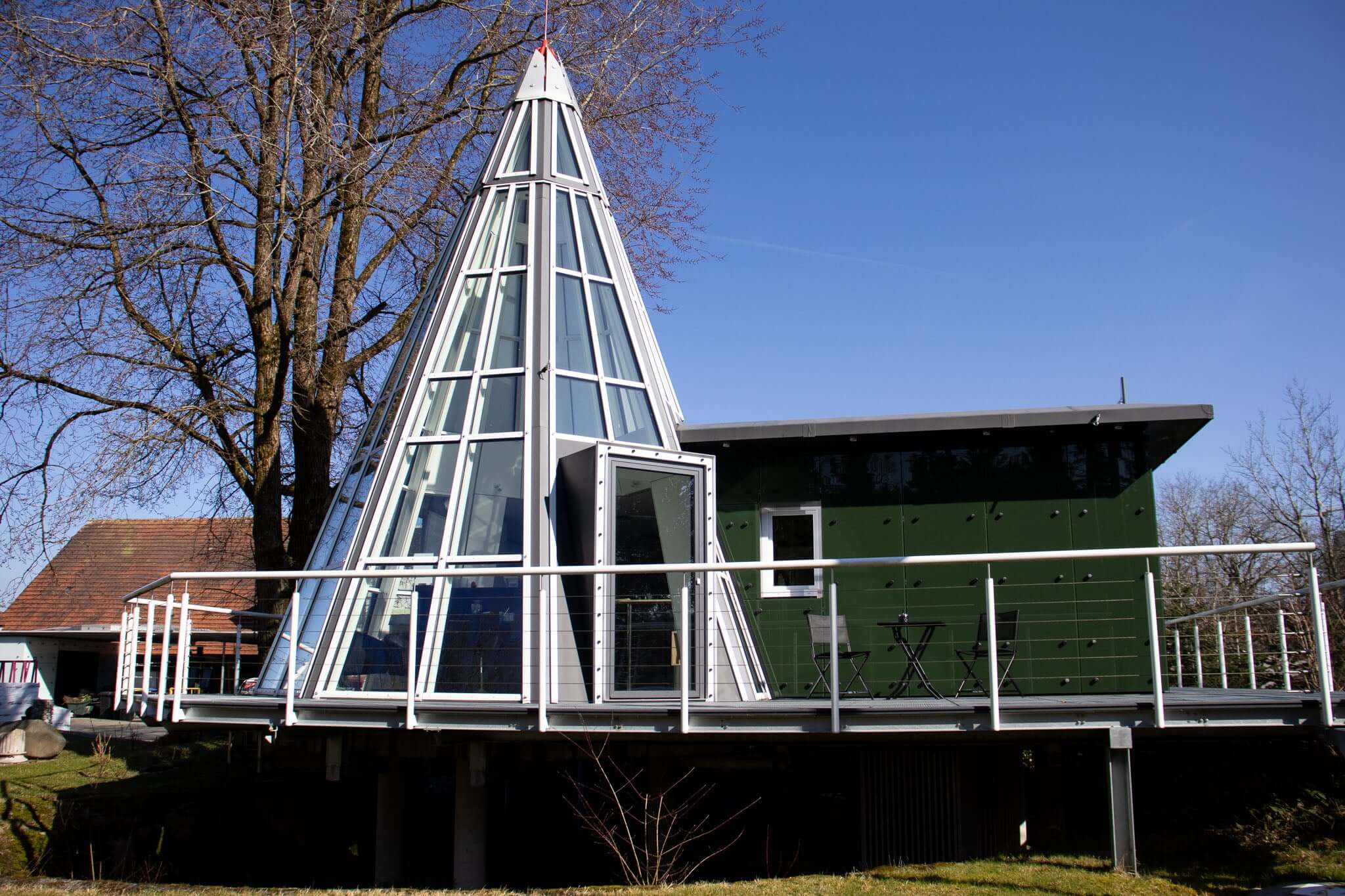 Unique triangular house with glass walls and green accents, set against a clear blue sky.