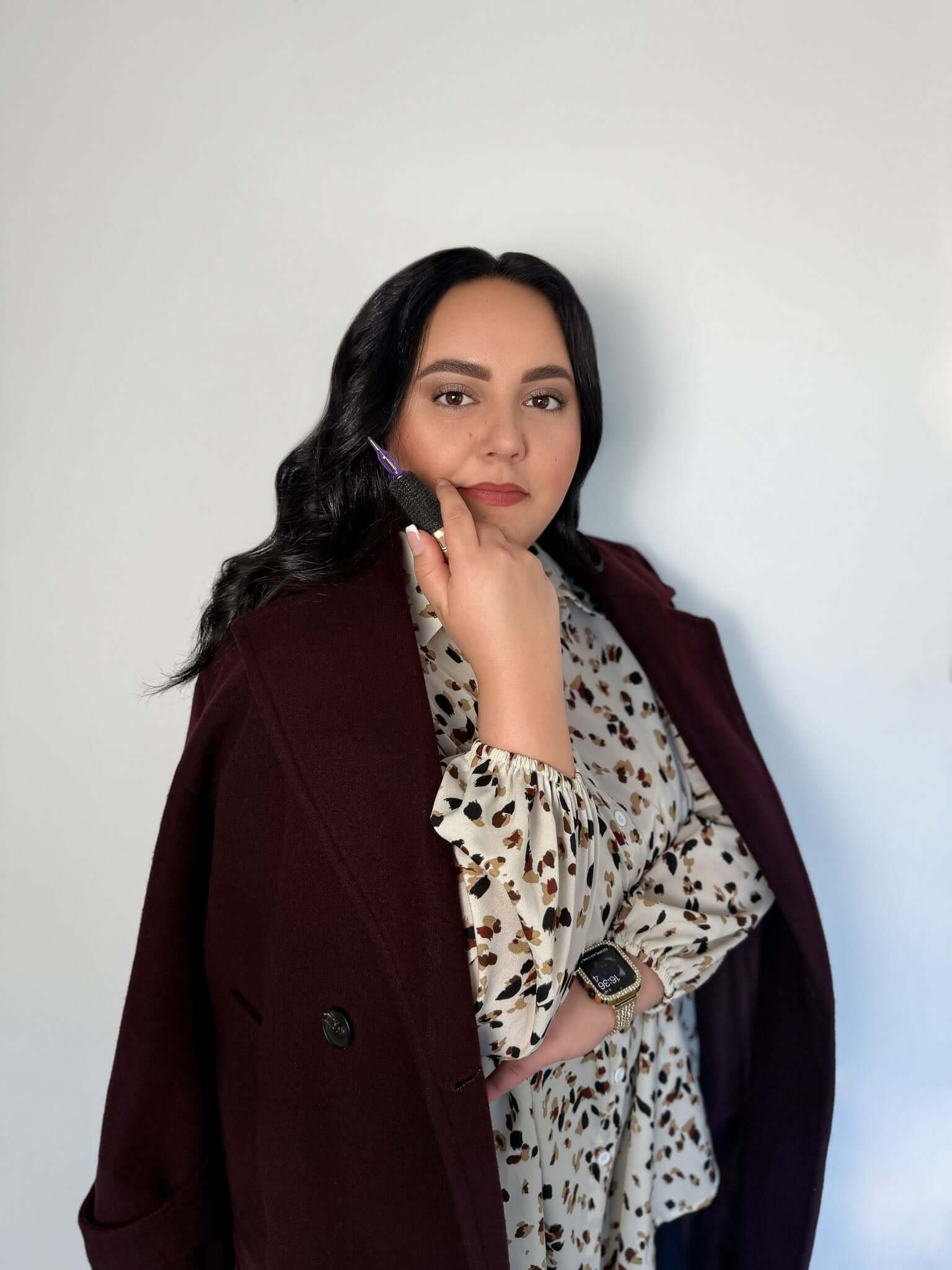 Confident woman posing in elegant attire with a maroon coat and floral blouse, showcasing style and poise.