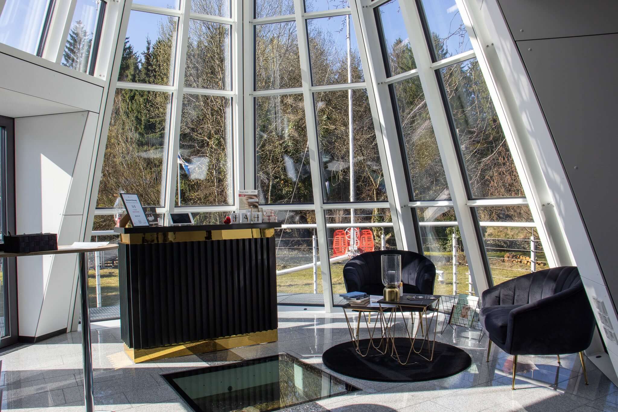 Modern lounge with large glass windows and stylish black furniture, offering a bright, inviting atmosphere.